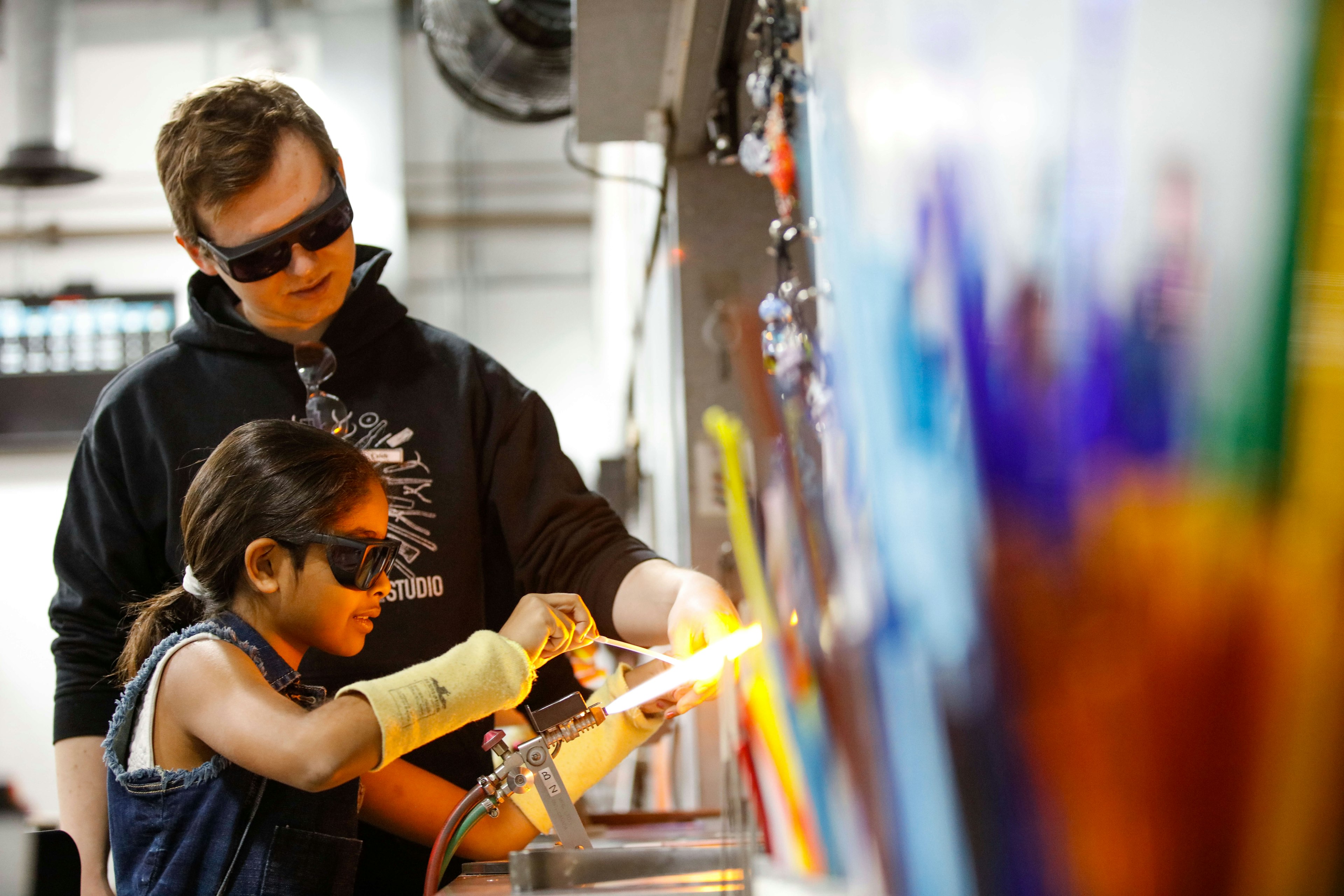 An adult and a kid wearing safety glasses during a Make Your Own Glass - Flameworking class at the Corning Museum of Glass in New York