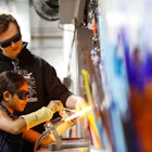 An adult and a kid wearing safety glasses during a Make Your Own Glass - Flameworking class at the Corning Museum of Glass in New York