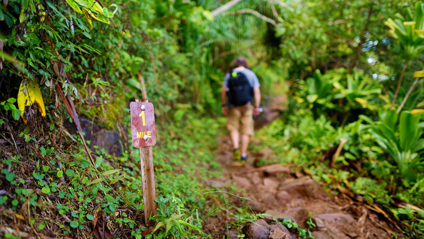 The mile-one sign on the Kalalau trail in Kauai, Hawaii, with a person hiking in the background