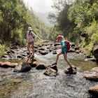 Mother and daughter crossing a creek, Na Pali Coast, Kauai, Hawaii.
