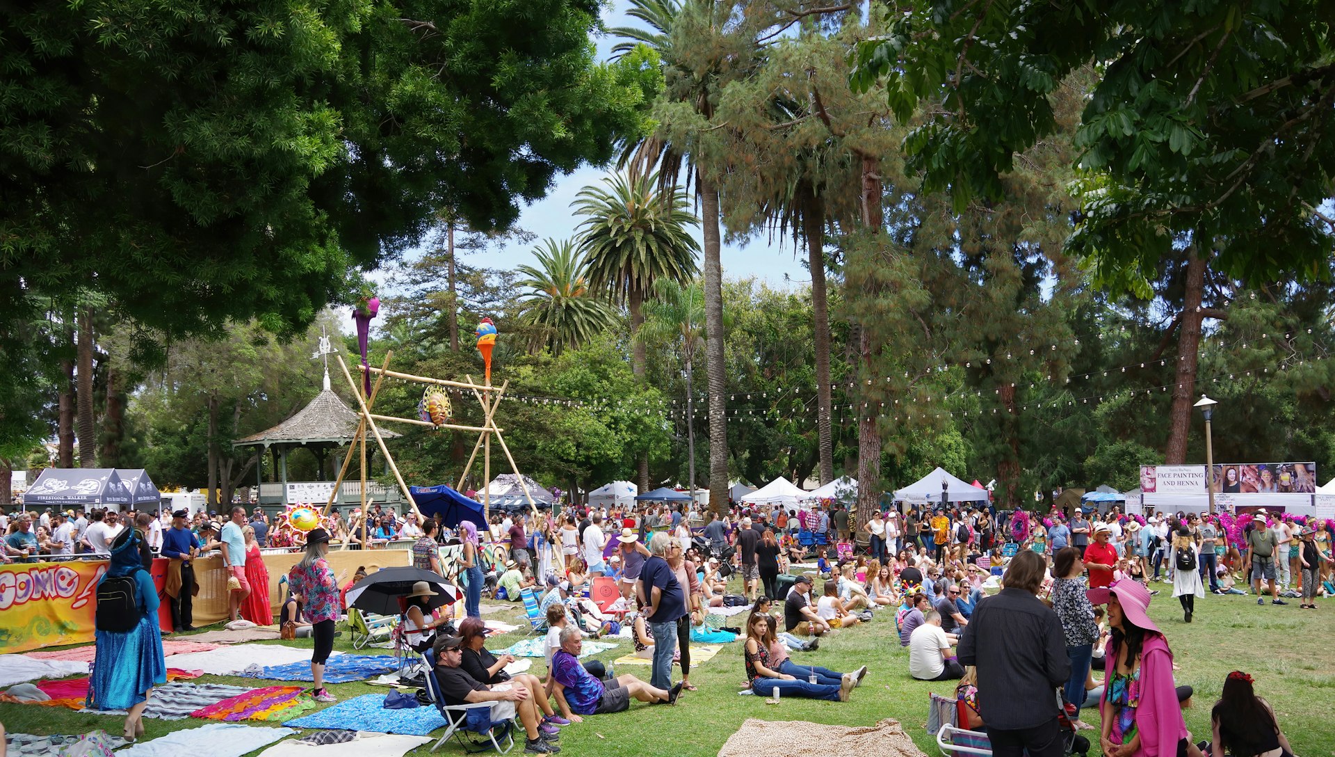 Lots of people gathered in groups, sitting on picnic blankets and relaxing at an outdoors event