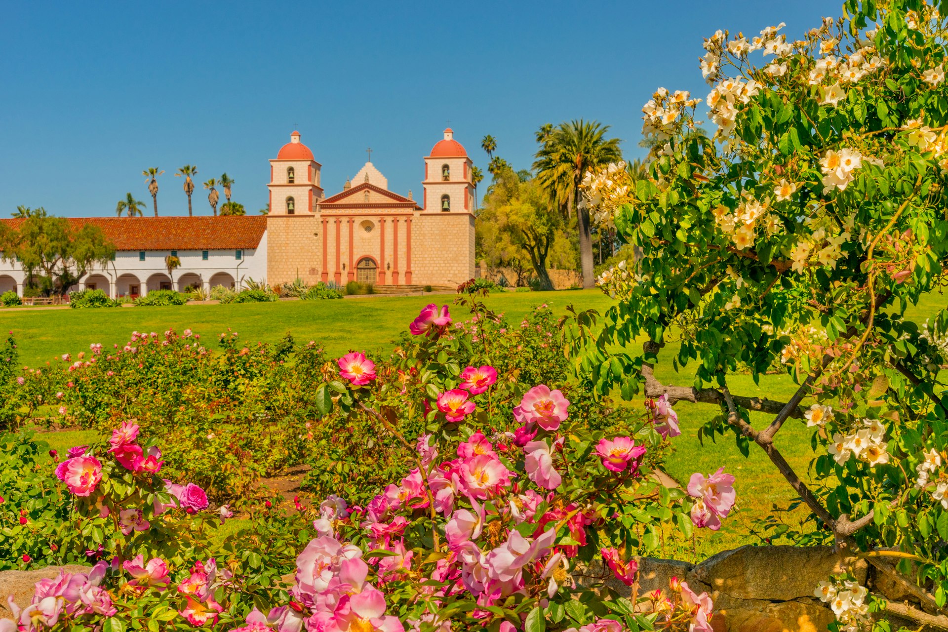 Flowers in bloom in pinks and yellows in the garden of a Spanish-style church building