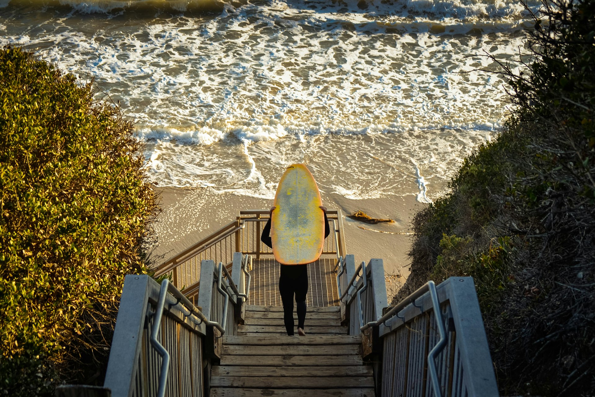 A shot of a surfer carrying a board down wooden steps to the ocean