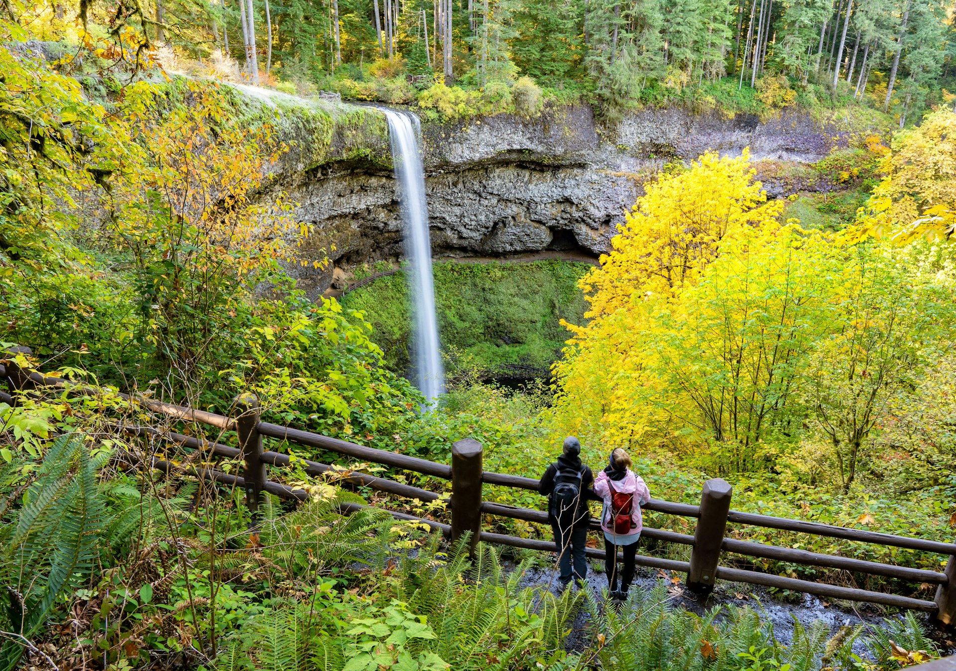 Two women looking at South falls and trees in autumn season showing fall colors, in Silver Falls State Park near Silverton, Oregon