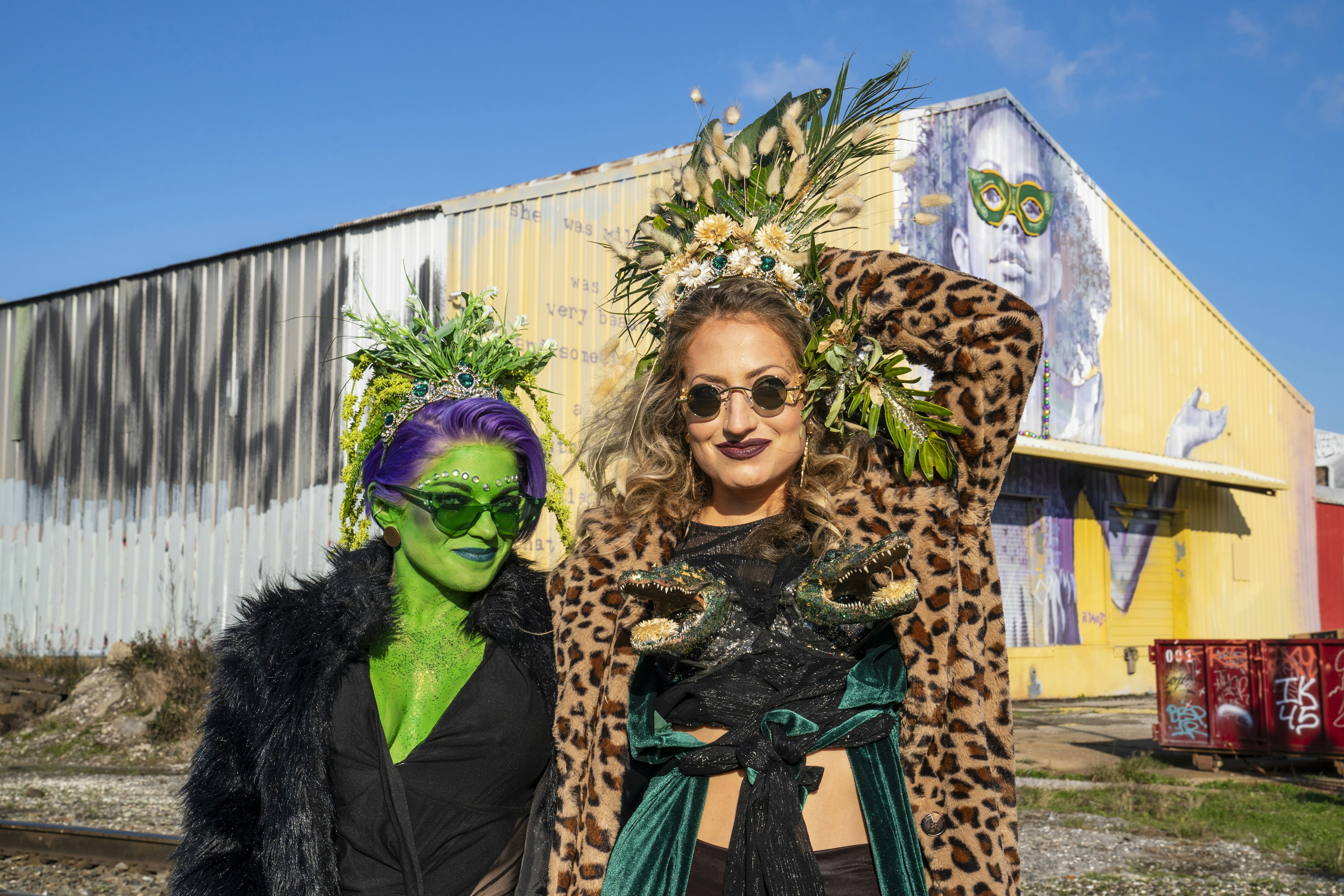Costumed revelers pose for a photo during Mardi Gras. One woman is painted green and the other is wearing leopard print. 