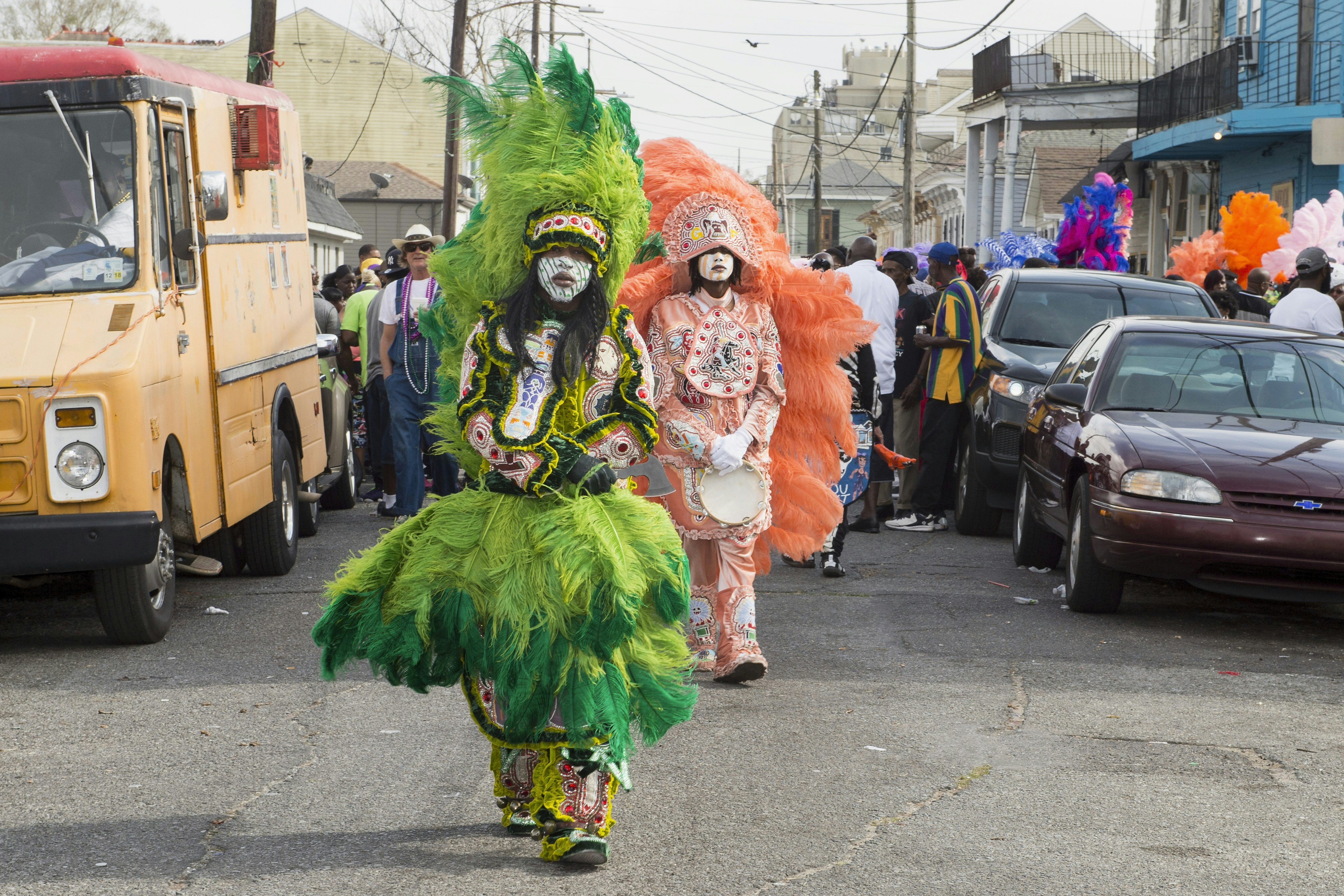 Two members of the Golden Eagles Mardi Gras Indians in elaborate beaded costumes walk through a city street. 