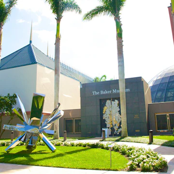 Stainless steel sculpture by artist Arik Levy titled RockGrowth 370, from 2017, in front of palm trees and main entrance to The Baker Museum, a modern art museum in Naples, Collier County, Florida, USA. The museum houses a diverse collection of art in a three-story, 30,000-square-foot facility. Permanent collections include American modernism, 20th-century Mexican art, sculpture and 3-dimensional art. The building, with its angled brick- and stone-toned fascia tiles, was designed by Florida architect Gene Aubry, who also designed the Hayes Hall building next to it.