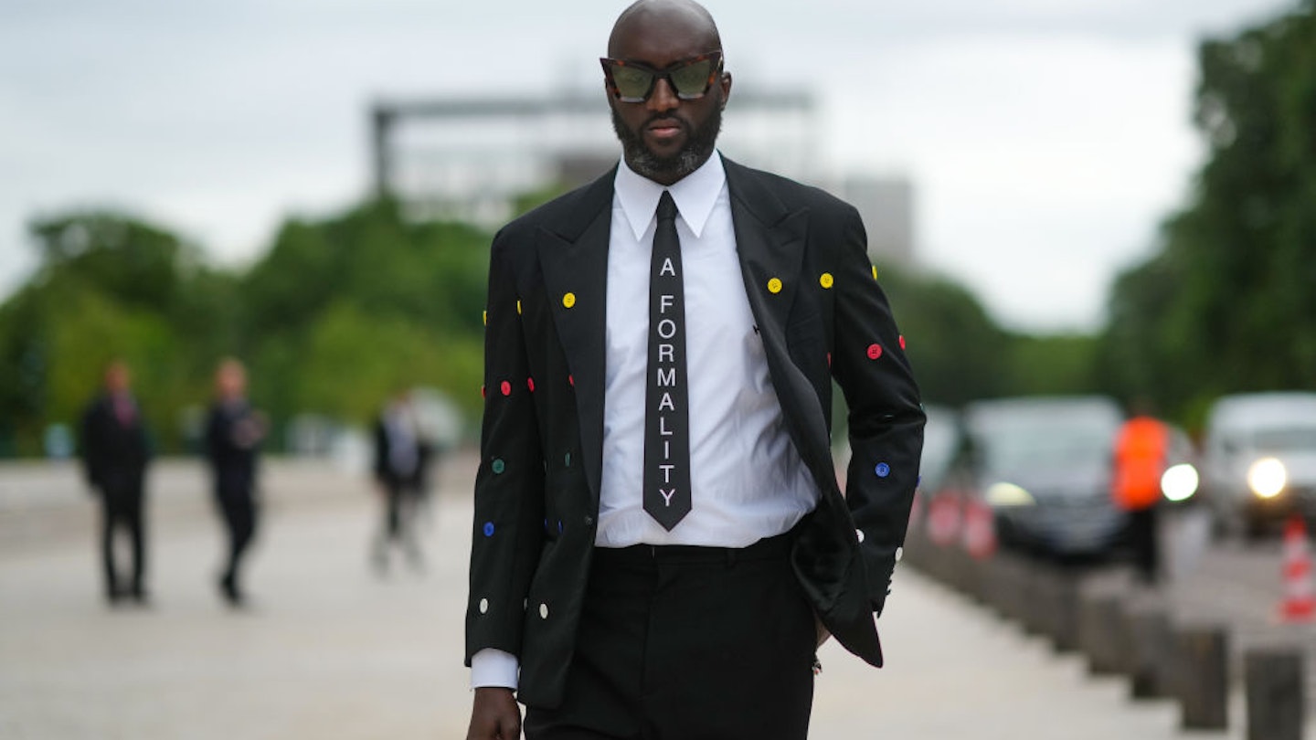PARIS, FRANCE - JULY 05: Virgil Abloh wears a white shirt, a black tie with 'A Formality' slogan, a black blazer jacket with multicolored buttons embroidered, black flared suit pants, a red ring, a gold watch, butterfly sunglasses, outside Louis Vuitton Parfum hosts dinner at Fondation Louis Vuitton, during Paris Fashion Week - Haute Couture Fall/Winter 2021/2022, on July 05, 2021 in Paris, France. (Photo by Edward Berthelot/Getty Images)