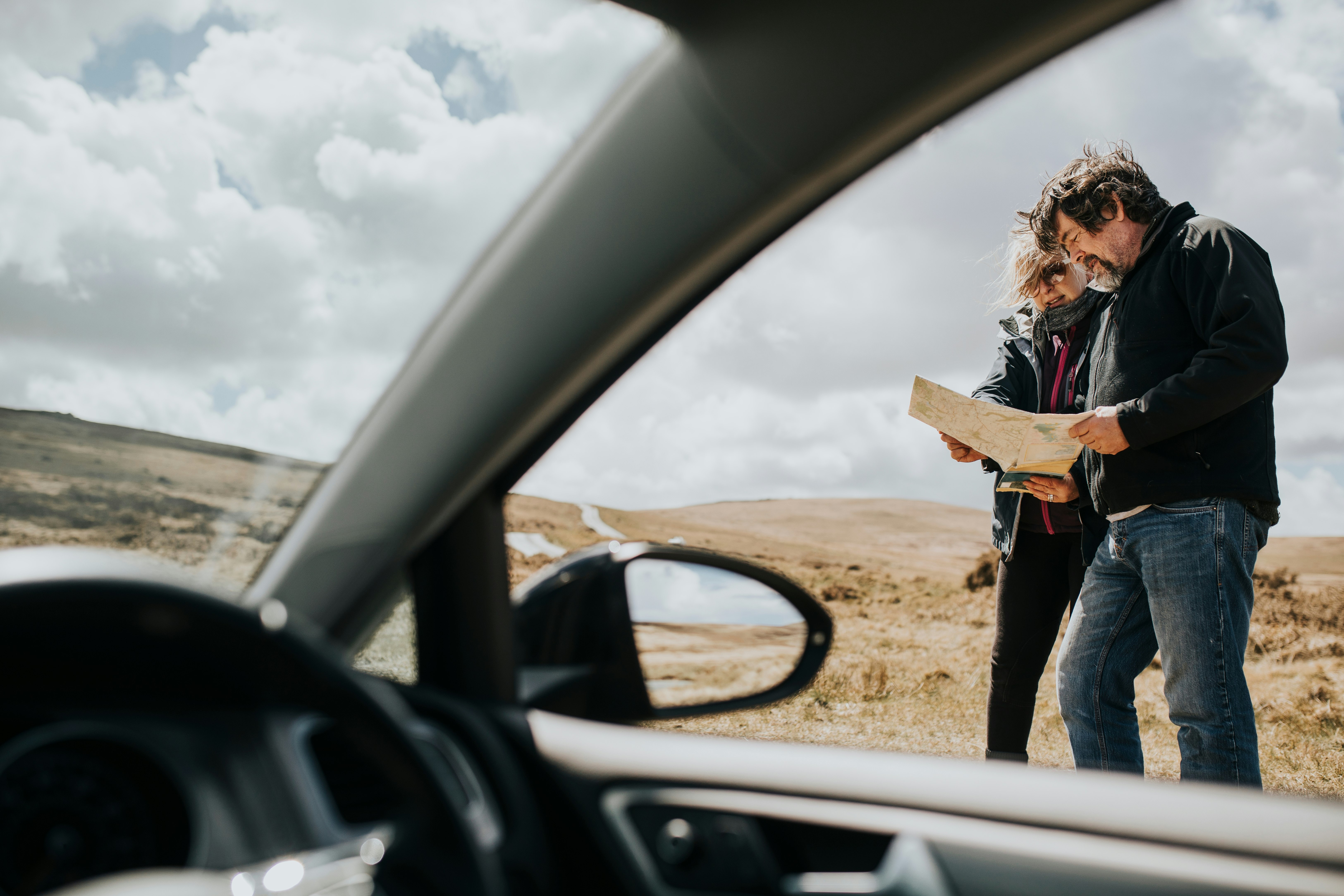 Senior tourist couple stand beside a car looking at a map 