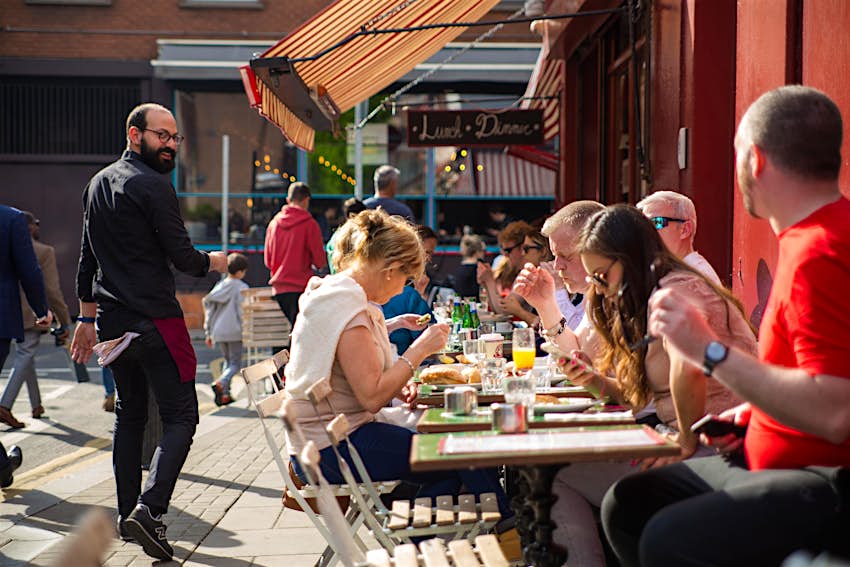 People dine at outdoor tables in the sun.