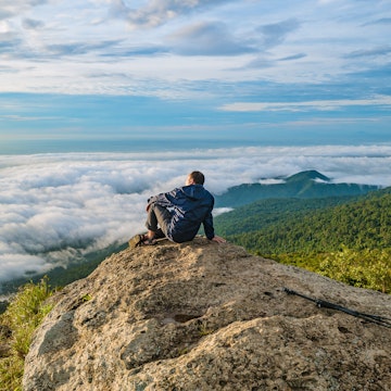 Asian men Sit on the cliff with beautiful sunrise sky on Khao Luang mountain in Ramkhamhaeng National Park,Sukhothai province Thailand