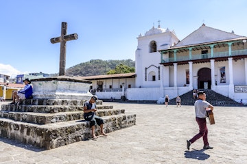 Santiago Atitlan, Lake Atitlan, Guatemala - March 8, 2019: Tourists visit the Catholic church & locals relax on steps & walk through the plaza in the largest town on Lake Atitlan in the Guatemalan highlands.