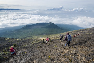 A group of western trekking tourists together with their local porters and guides descencing from the crater rim of Nyiragongo Volcano in Virunga National Park in January 2016.