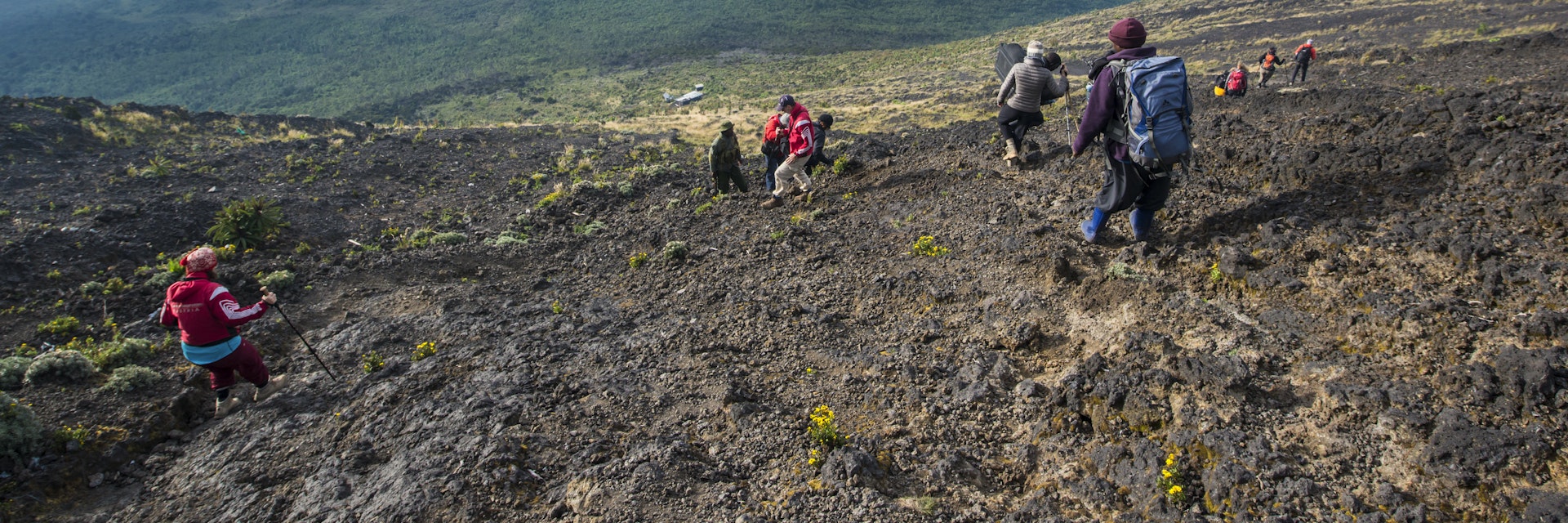 A group of western trekking tourists together with their local porters and guides descencing from the crater rim of Nyiragongo Volcano in Virunga National Park in January 2016.