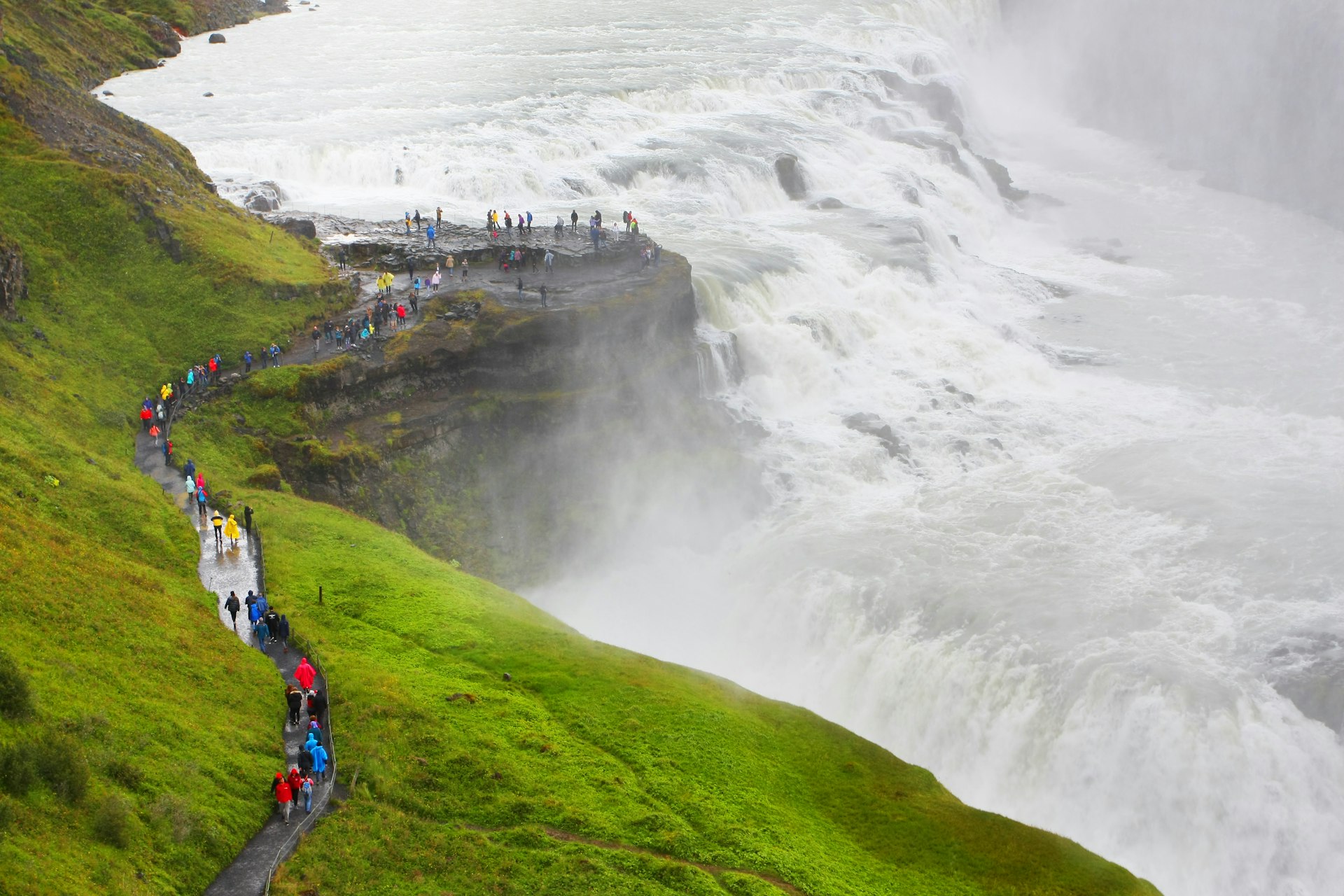 Visitors walking along a dirt path at the Cascades of Gullfoss waterfall, seen from above