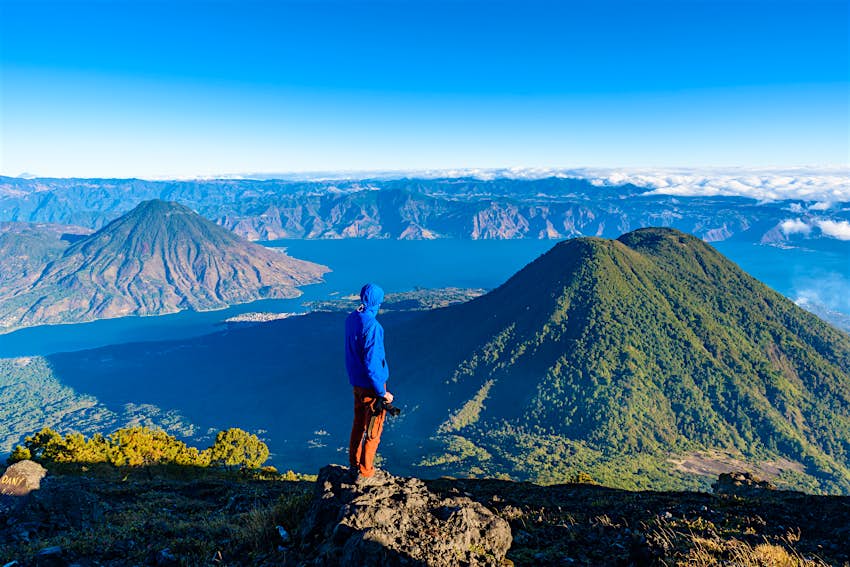 Hiker with panorama view of Lake Atitlán and volcano San Pedro and Toliman early in the morning from peak of volcano Atitlán, Guatemala