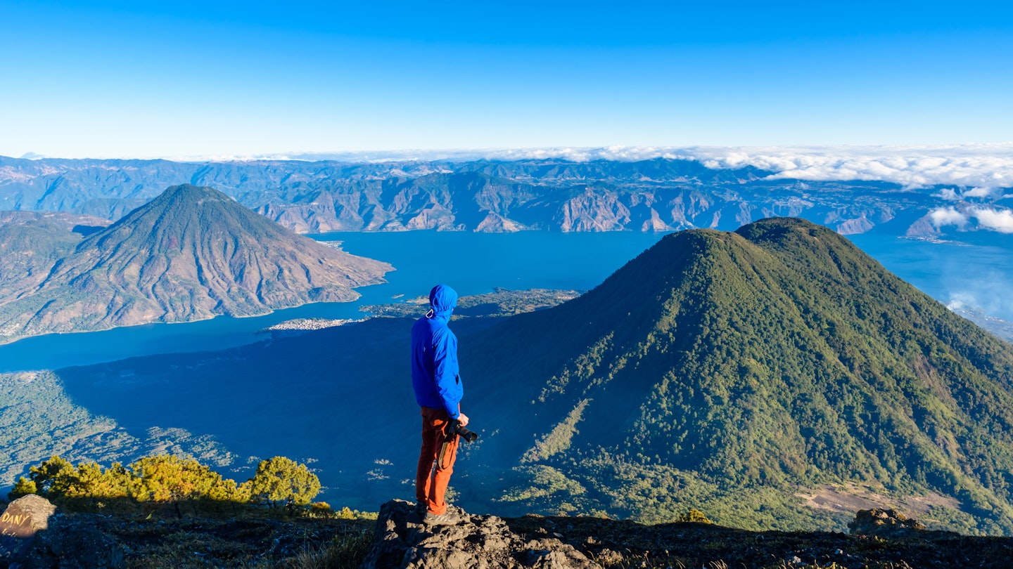Hiker with panorama view of Lake Atitlan and volcano San Pedro and Toliman early in the morning from peak of volcano Atitlan, Guatemala. Hiking and climbing on Vulcano Atitlan.