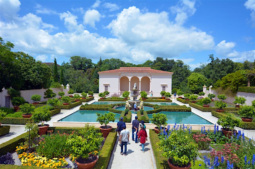 Tourists stroll around an Italian-style garden, with individual flower beds separated by low hedges