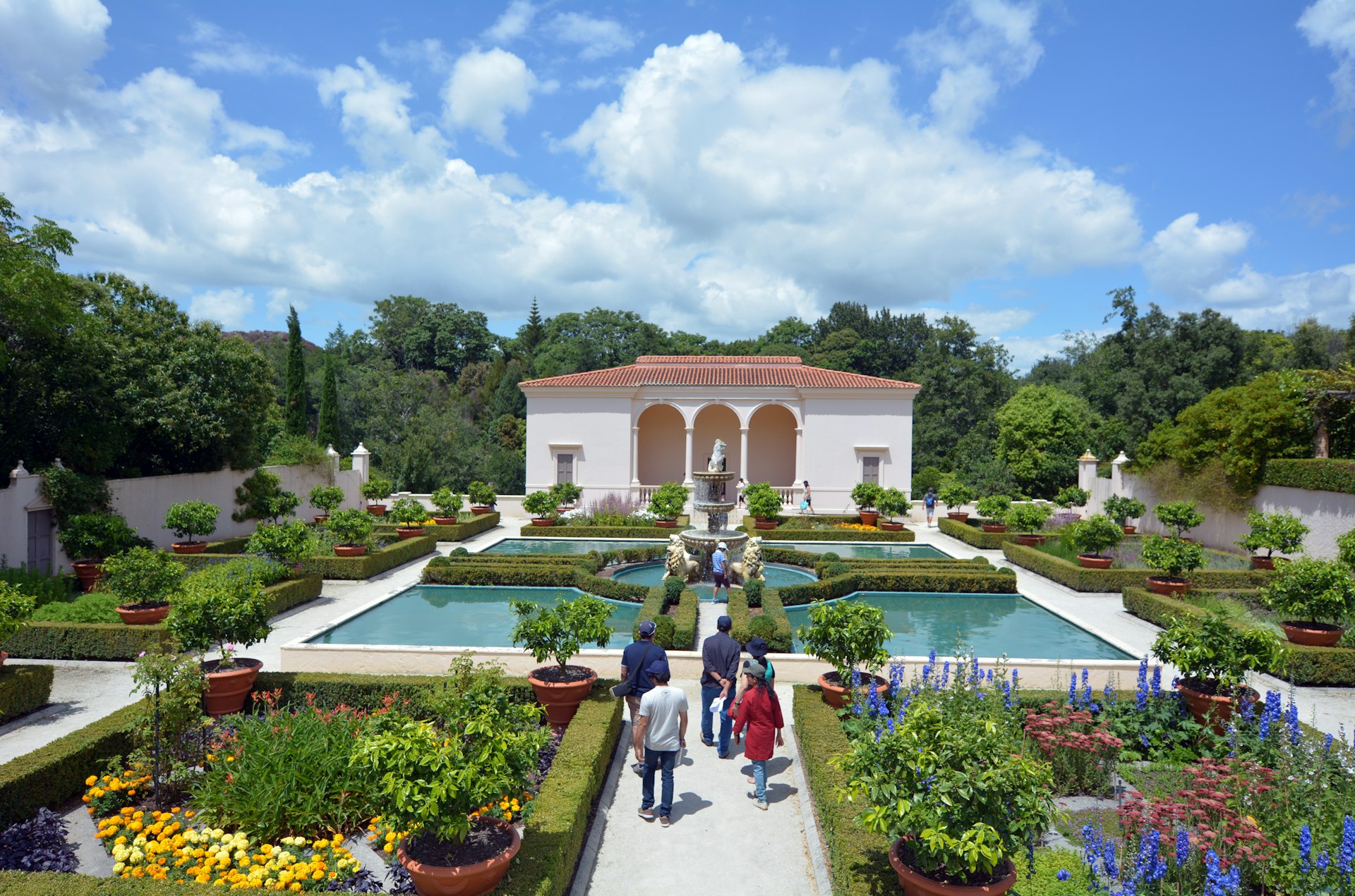 Tourists stroll around an Italian-style garden, with individual flower beds separated by low hedges