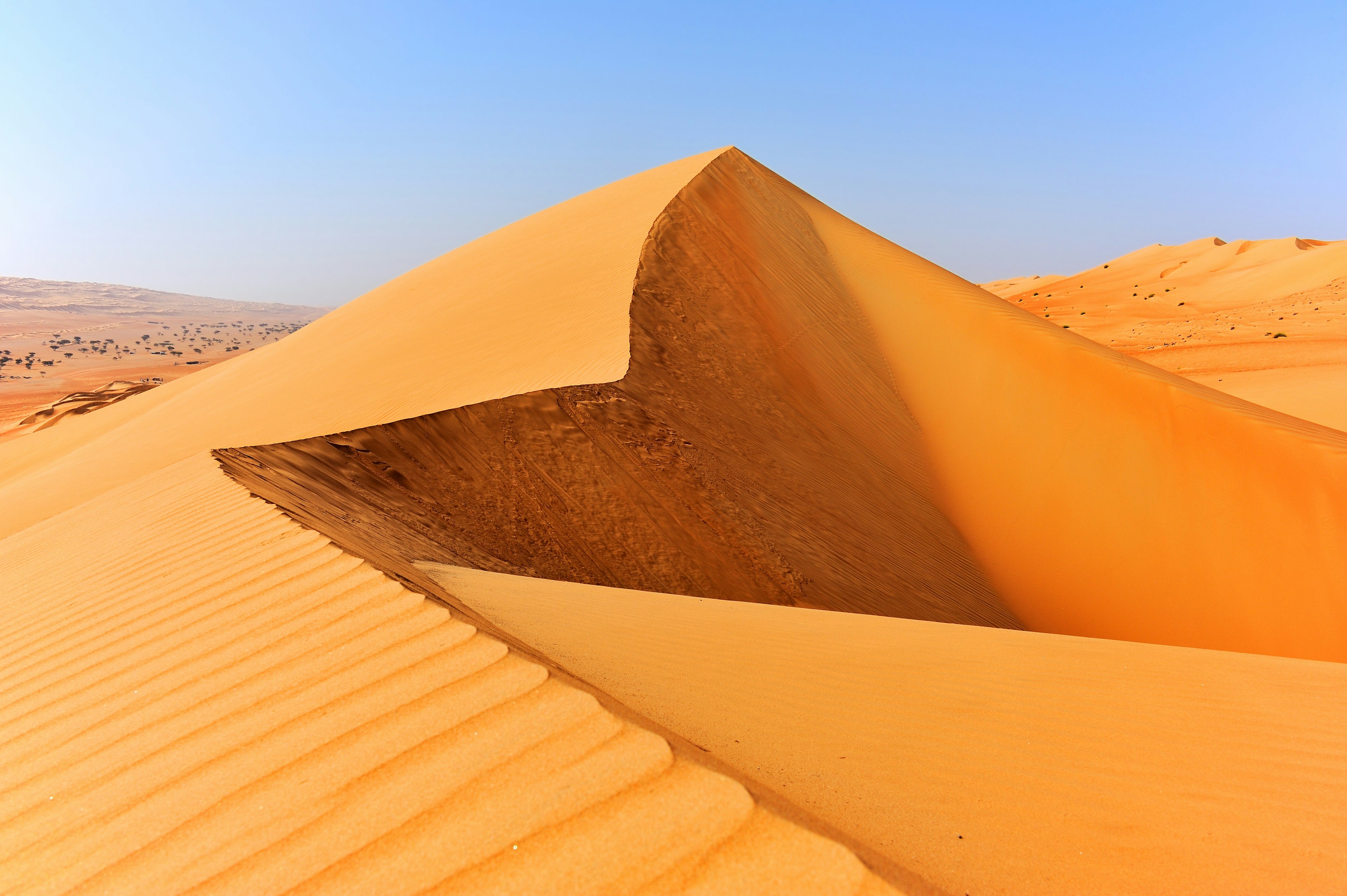 Sun hits golden sand against a blue sky on the geometric formations of the Sharqiya Sands dune