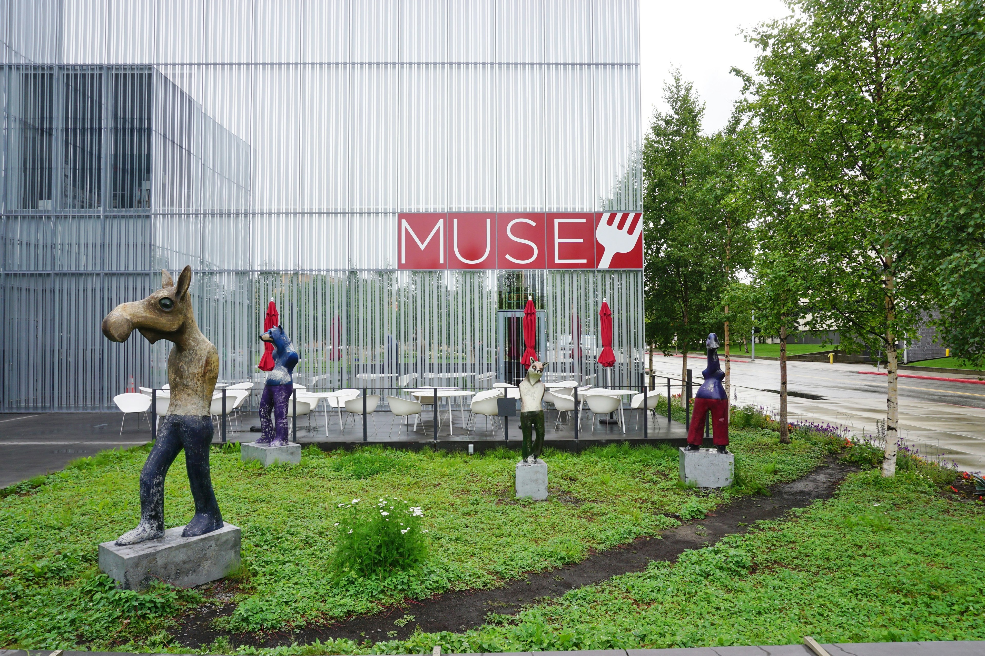 A figural sculpture with a moose head and other outdoor art on a lawn in front of the Anchorage Museum