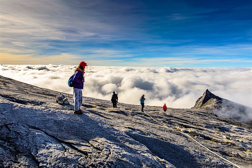 Trekkers walk above the cloud line on the rocky summit of Mt Kinablu's south peak. 