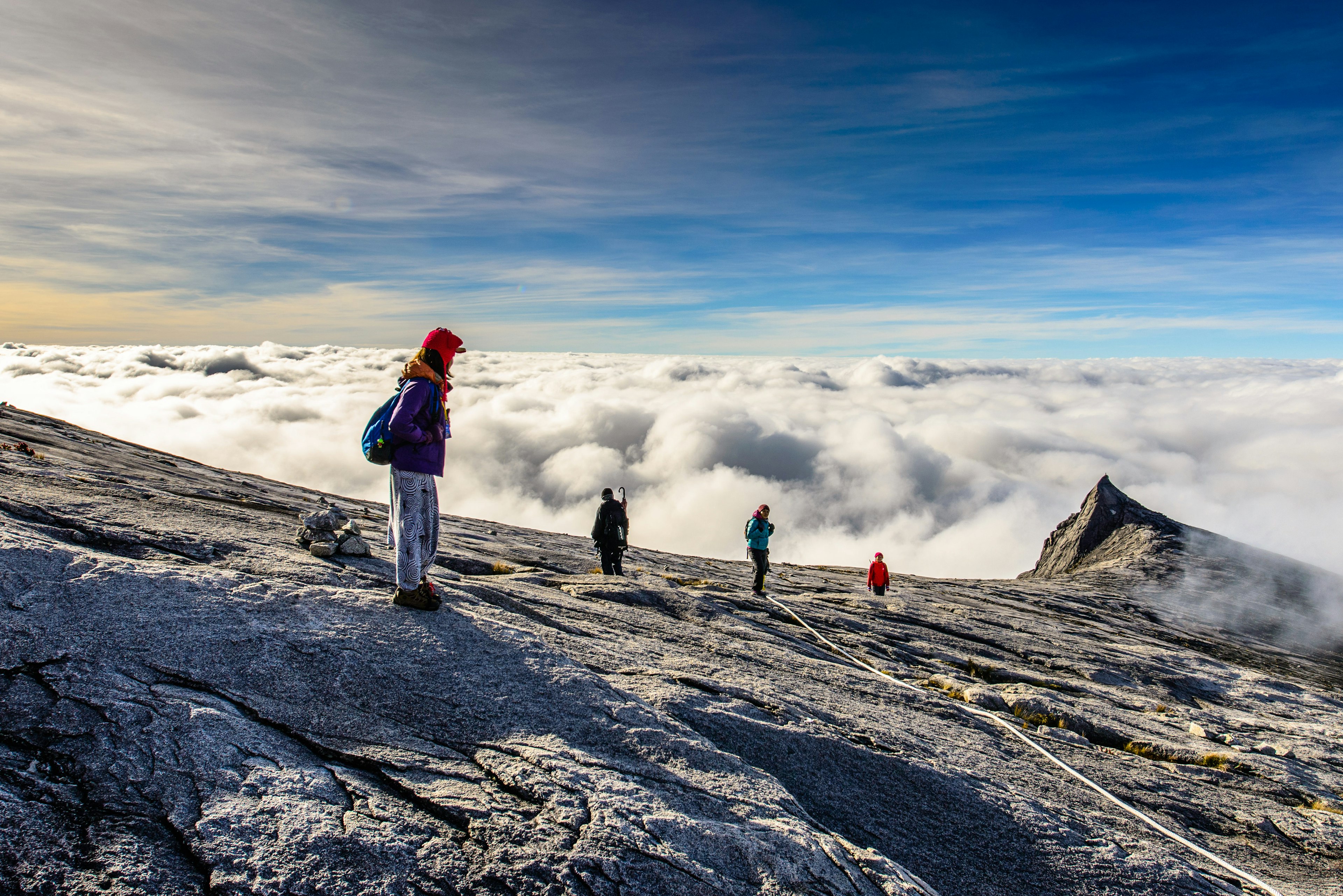 Trekkers walk above the cloud line on the rocky summit of Mt Kinablu's south peak.