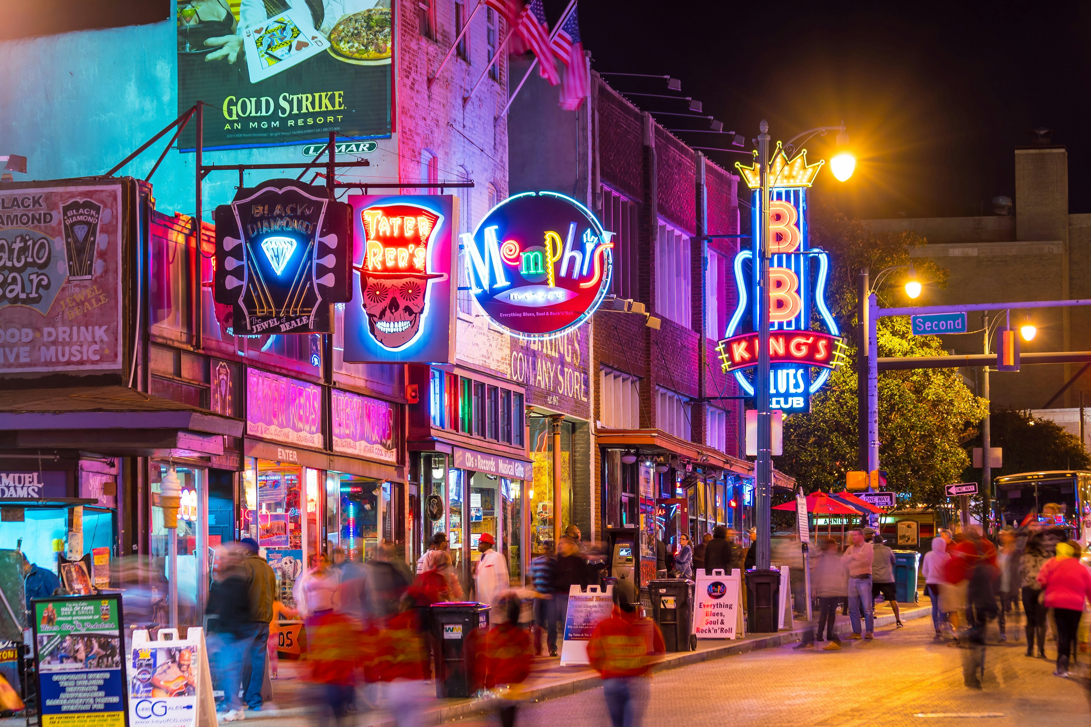 People walk down a street in the evening lined with neon signs