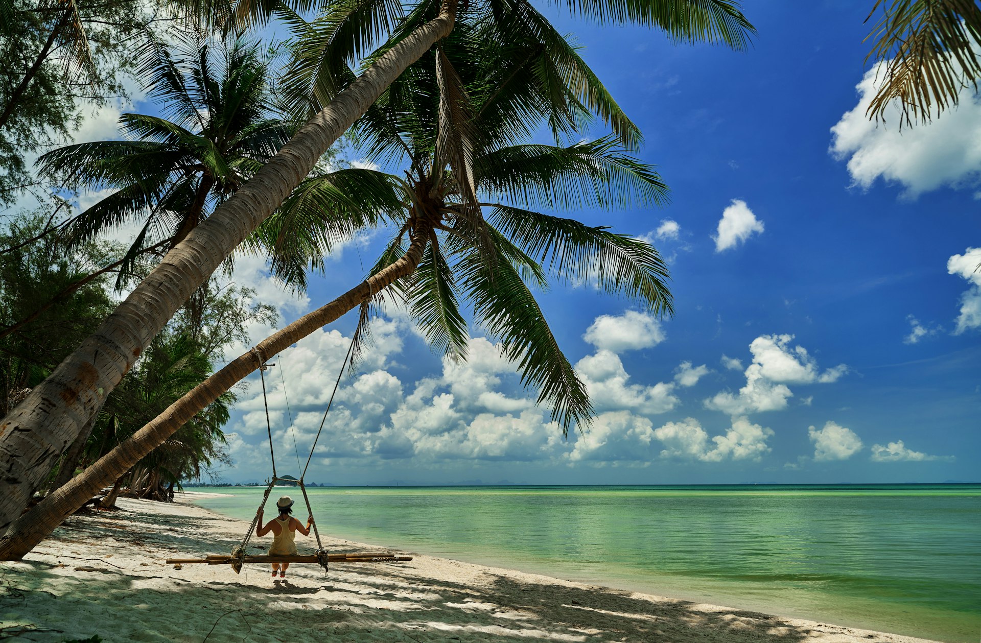 A woman sits on a swing suspended from a palm on a beach in Koh Samui