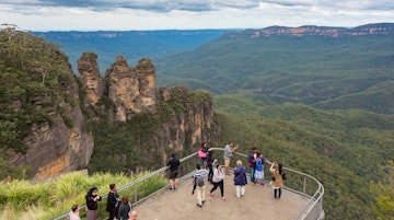 Blue Mountains, Australia - May 1, 2016: People at observation deck at Echo point lookout with view of famous Three Sisters mountains and Blue Mountains eucalyptus forest