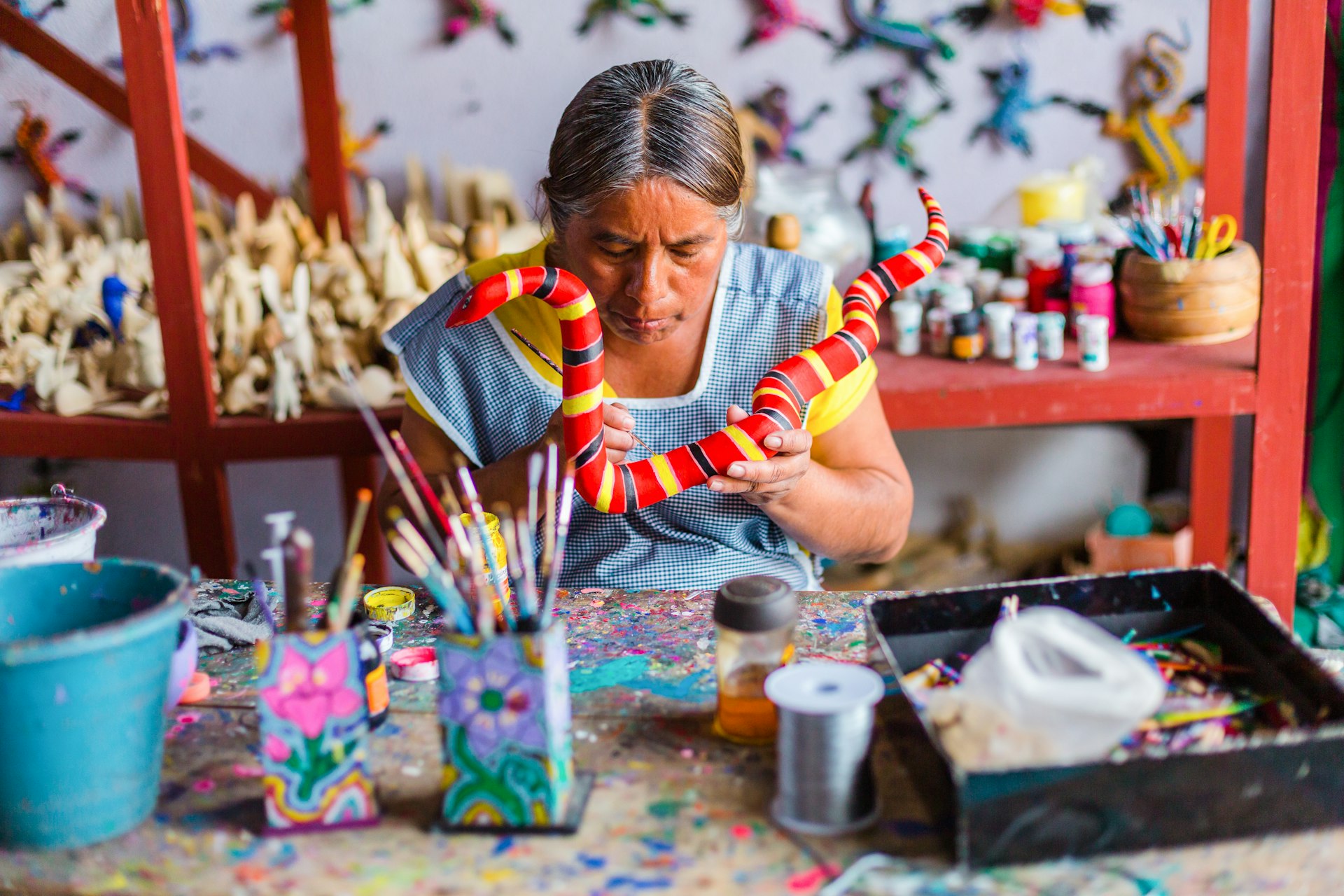 An artist paints a colorful carved-wood alebrije sculpture in a studio in San Martin Tilcajete