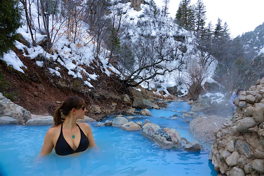 CLOSE UP: Female traveler relaxes in the soothing hot water of Fifth Water Springs in Utah. Young Caucasian woman in a black bikini stands in a stunning turquoise pond and observes the snowy nature.; Shutterstock ID 1539628718; your: Brian Healy; gl: 65050; netsuite: Online Editorial; full: Best free things to do in Utah