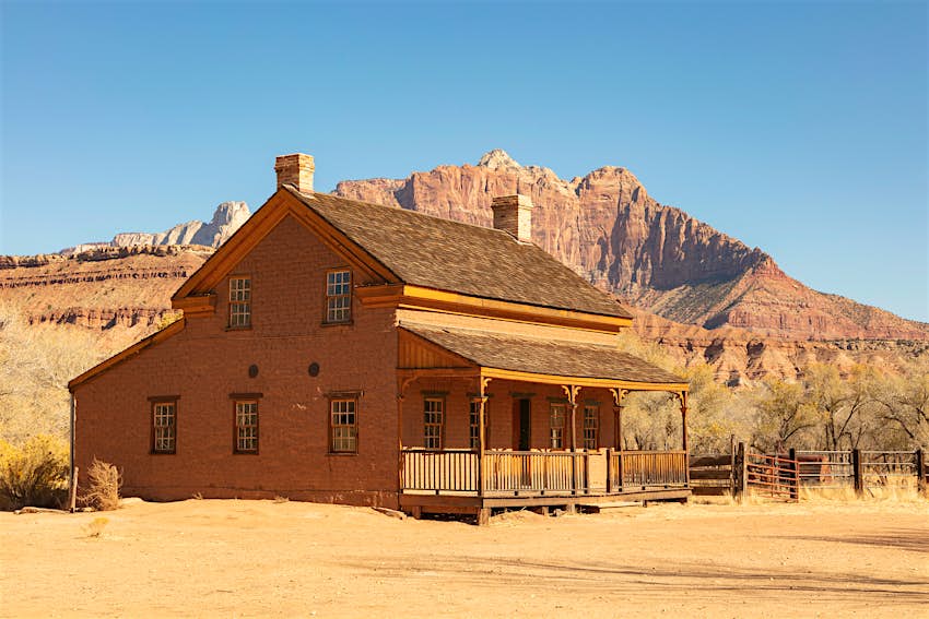 An abandoned house and picket fence against rock formations and a blue sky at Grafton ghost town, Utah