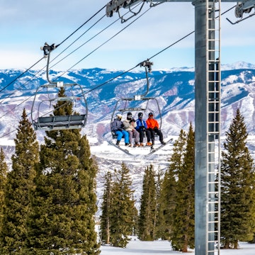 Skiers and snowboarders ascend the Alpine Springs chairlift at the Aspen Snowmass ski resort, in the Rocky Mountains of Colorado on a partly cloudy winter day. 