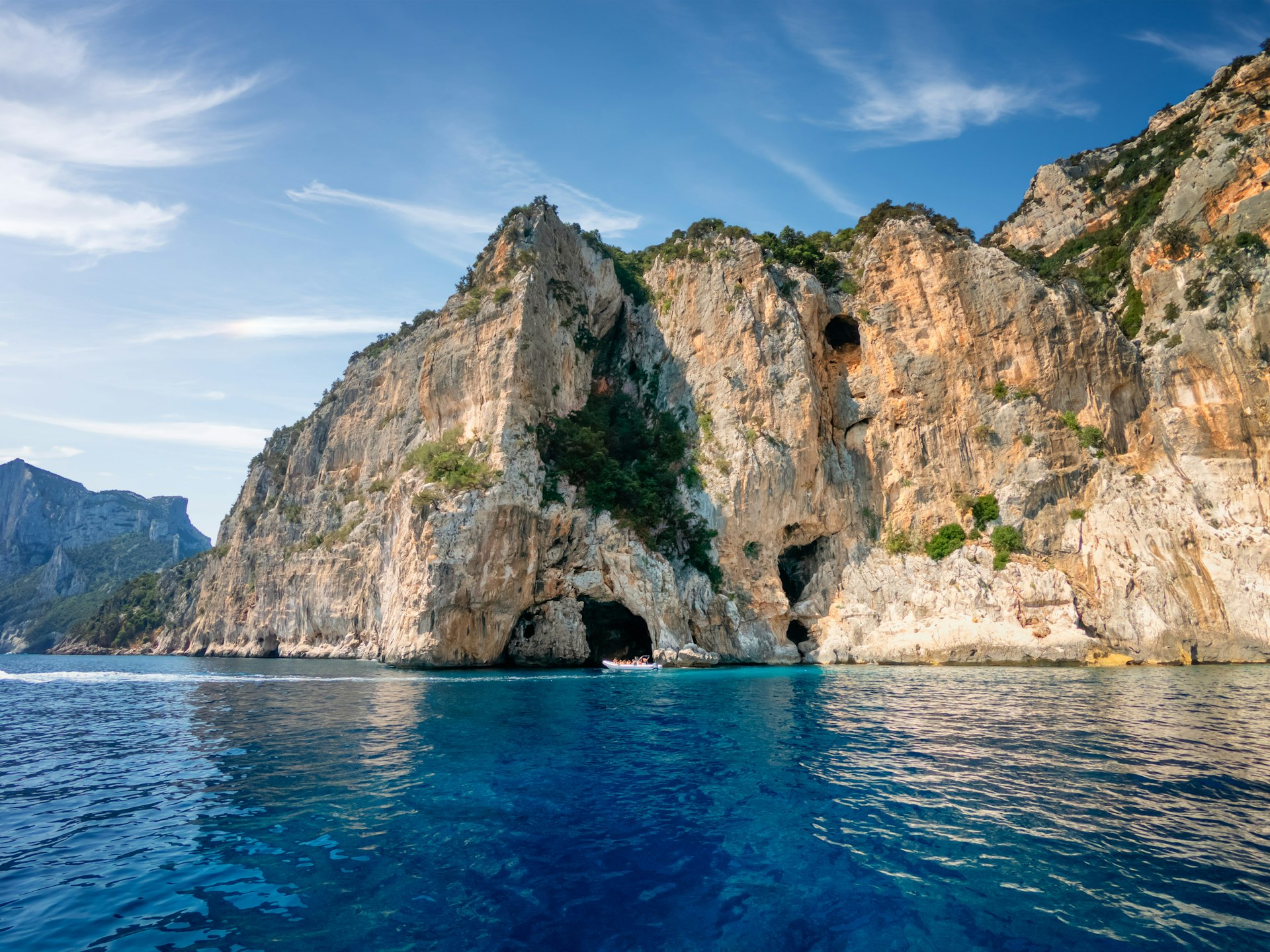 A rocky limestone cliff rises above a clear blue sea. 