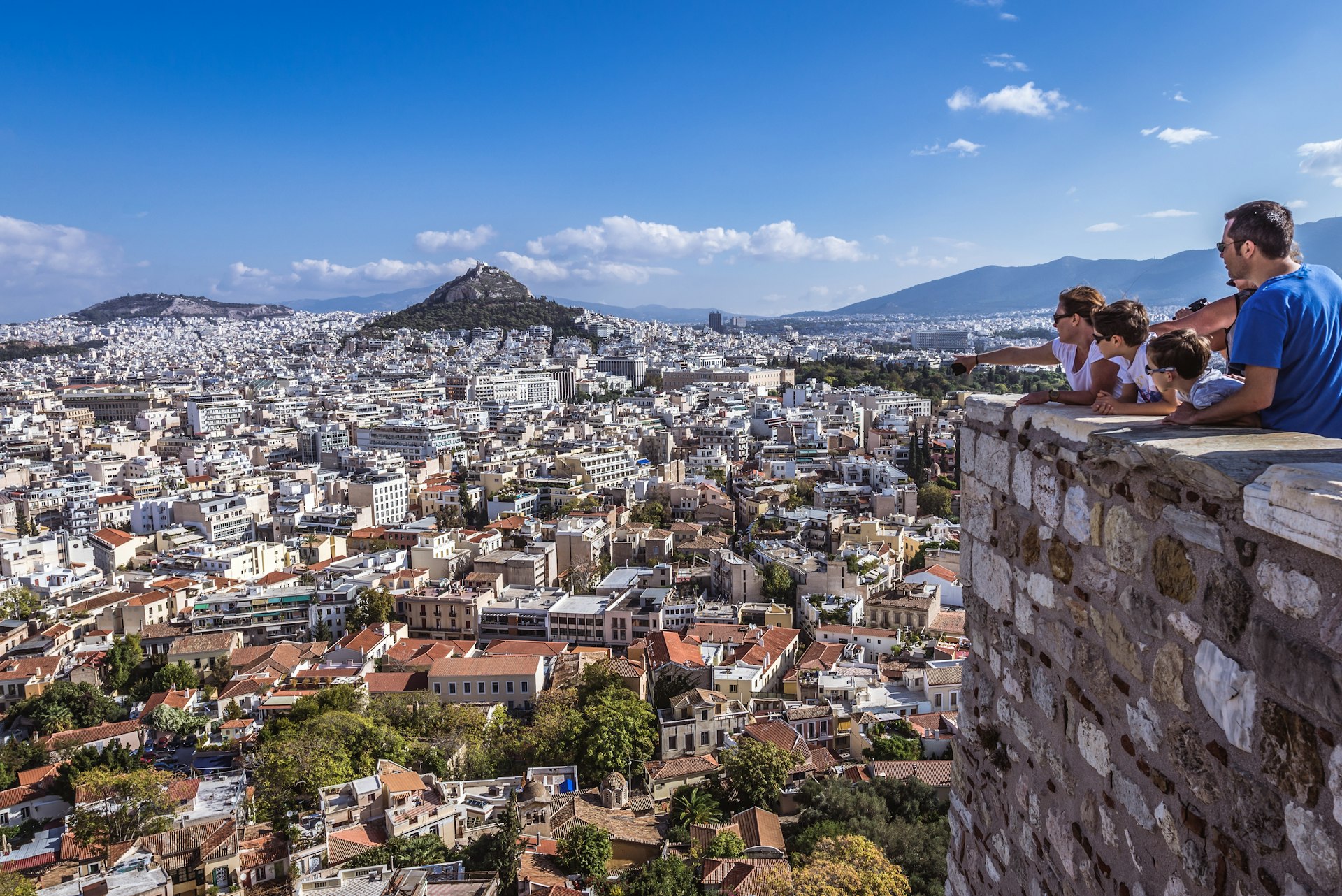 A family looks out on Lycabettus Mountain from a hill of the Acropolis citadel in Athens