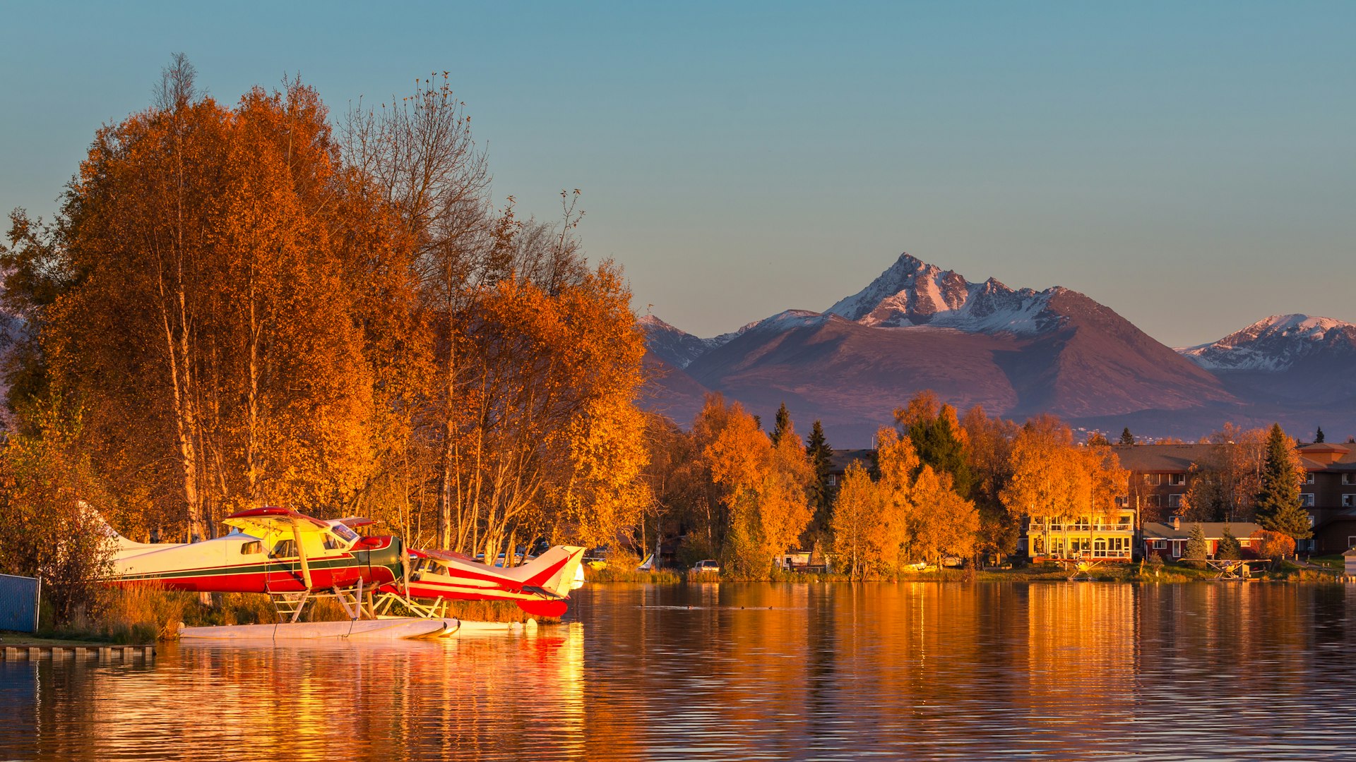 Seaplanes floating in Spenard Lake at sunset with houses and mountain peaks in the distance