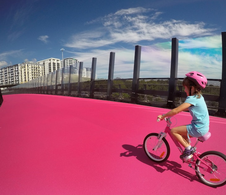 Happy young girl (age 07) ride a bike on  bright pink cycleway in Auckland, New Zealand. Real people. Copy space; Shutterstock ID 613004390; your: Brian Healy; gl: 65050; netsuite: Lonely Planet Editorial; full: Free things to do in Auckland