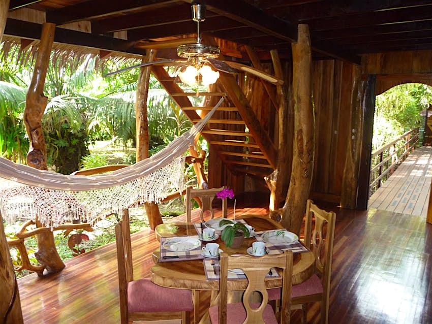 Interior shot of the wooden floors and paneling at the Topos Tree House in Costa RIca. There is a wooden table and chairs in the middle of the room and a white canopy off to the left. 