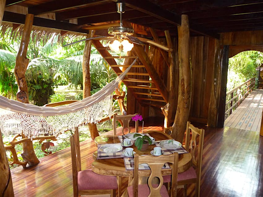 Toma interior de los pisos y paneles de madera de la Casa del Árbol Topos en Costa Rica.  Hay una mesa y sillas de madera en el medio de la habitación y un toldo blanco a la izquierda. 