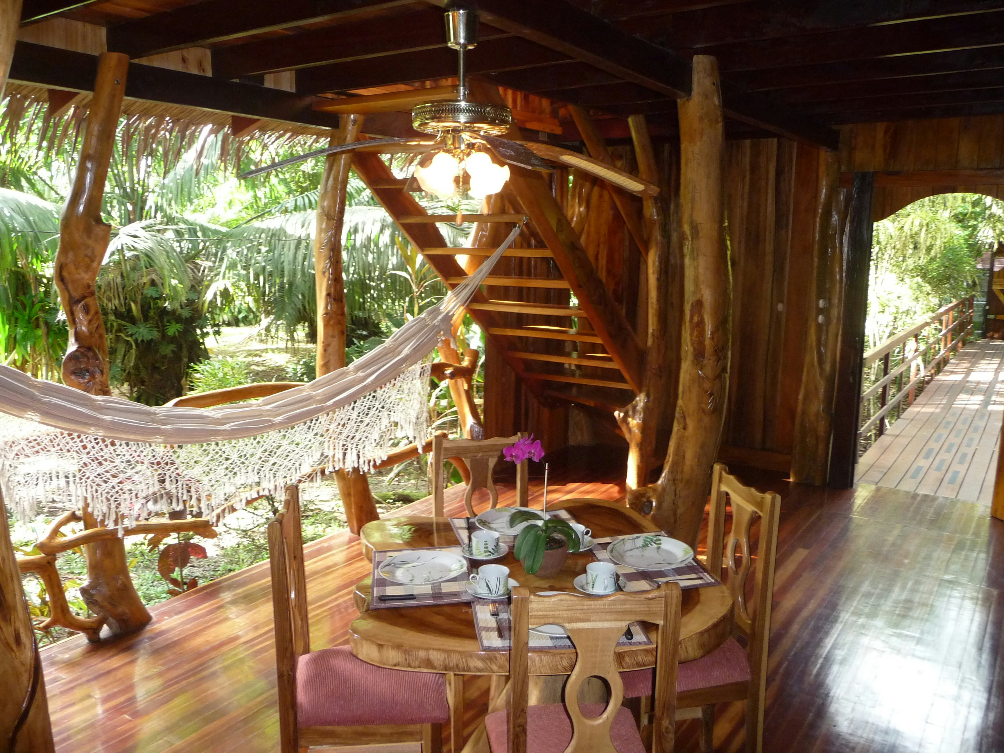 Interior shot of the wooden floors and paneling at the Topos Tree House in Costa RIca. There is a wooden table and chairs in the middle of the room and a white canopy off to the left.