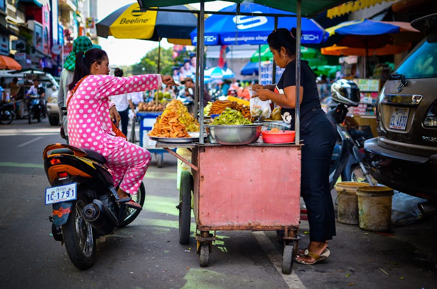 Women on a scooter eating street food in Phnom Penh, Cambodia 