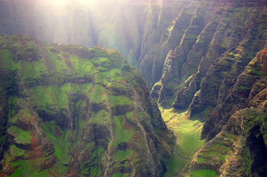 An aerial shot of cliffs plunging to the lush Nualolo Valley in Kauaʻi