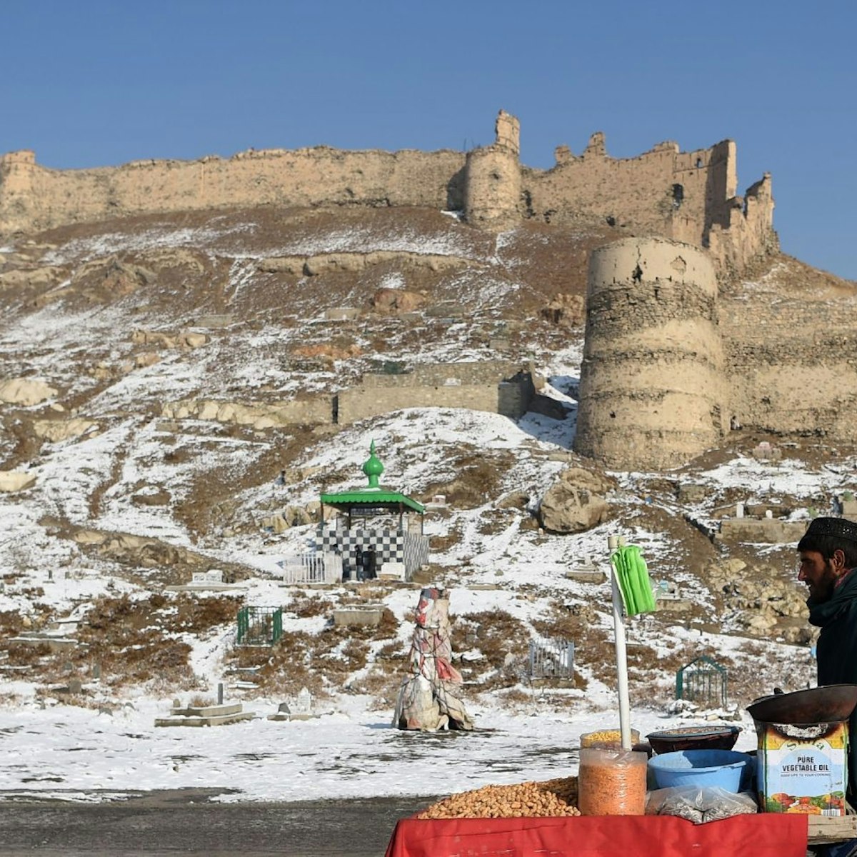 TOPSHOT - An Afghan vendor pushes a wheelbarrow after the first snowfall near the old fortress of Bala Hissar in Kabul on December 15, 2017. / AFP PHOTO / WAKIL KOHSAR        (Photo credit should read WAKIL KOHSAR/AFP via Getty Images)