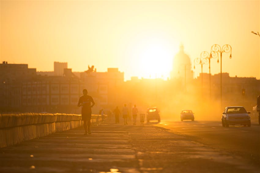 Les coureurs et les voitures passent au lever du soleil sur le Malecon dans la vieille Havane, Cuba
