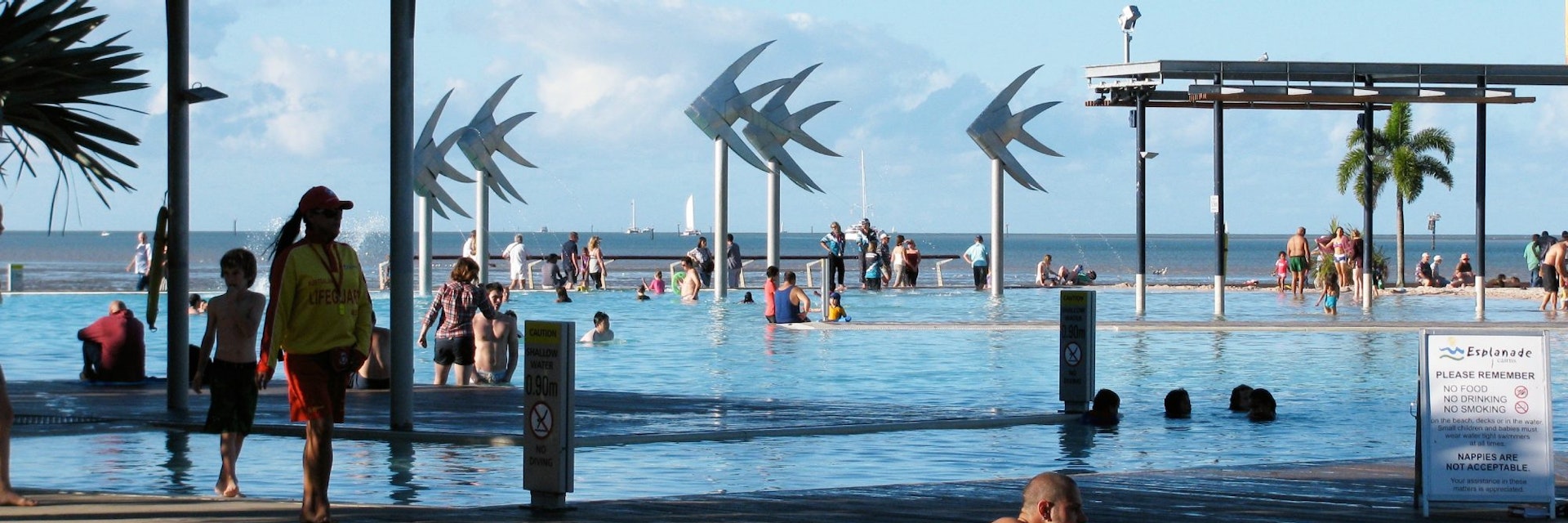 People by the pool at the Cairns Esplanade Lagoon with the fish sculptures in the background in Cairns, Queensland, Australia.