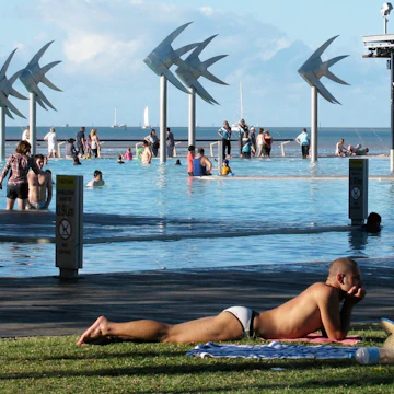 People by the pool at the Cairns Esplanade Lagoon with the fish sculptures in the background in Cairns, Queensland, Australia.