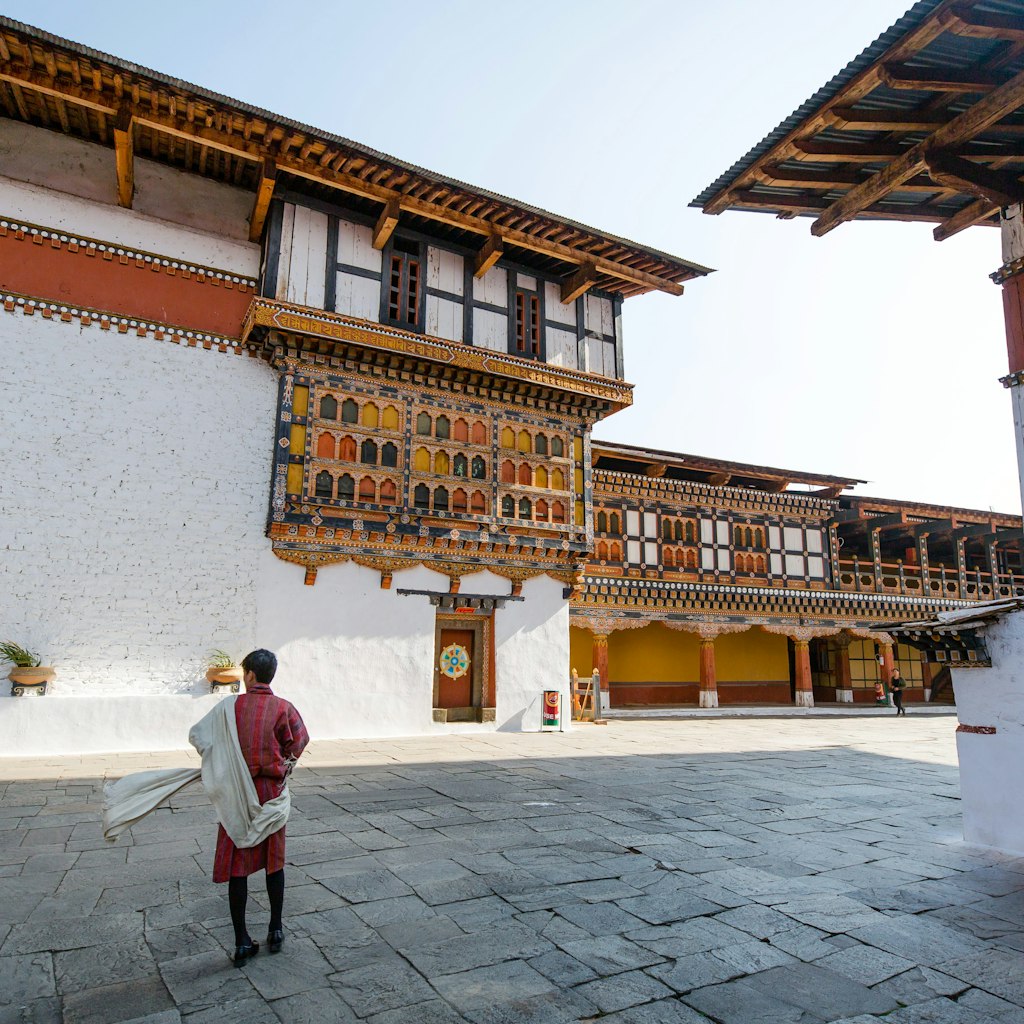 A local guide standing still while wearing a traditional clothing for men called Gho a knee length and kimono-like cloth held in place by a belt called Kera. Rinpung Dzong is an architectural feat housing a network of courtyards, temples and offices. Its full name is Rinche Pung Dzong which literally means Fortress on a Heap of Jewels.