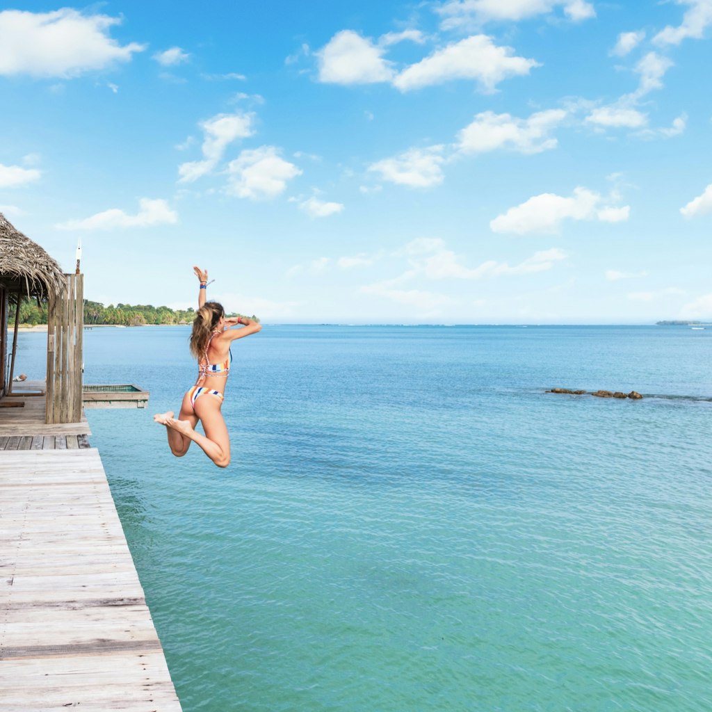A woman jumps off a wooden platform into the blue waters in Bastimentos, Bocas Del Toro Panama. 