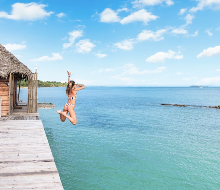 A woman jumps off a wooden platform into the blue waters in Bastimentos, Bocas Del Toro Panama. 